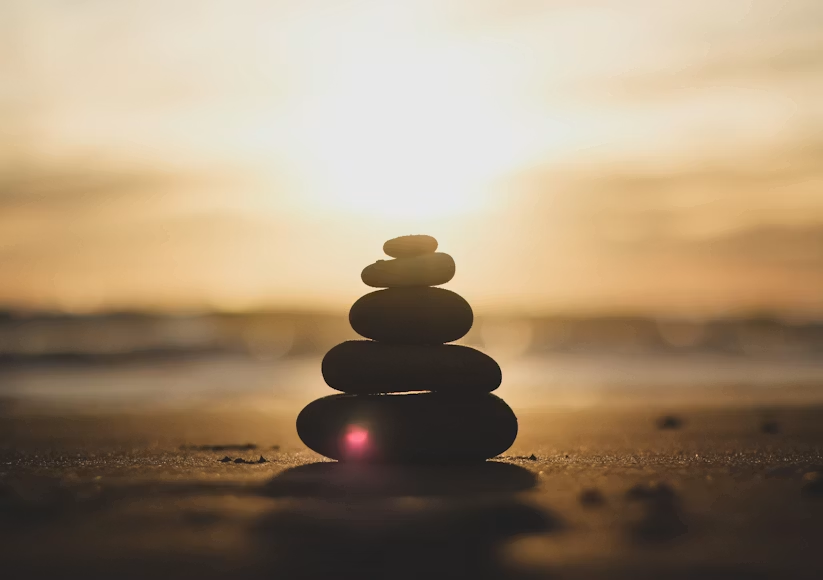  Silhouette of stacked balanced stones on a sandy beach against a warm golden sunset sky.