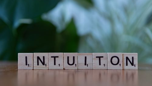 Wooden scrabble tiles spelling the word intuition on a reflective surface with green foliage in background.
