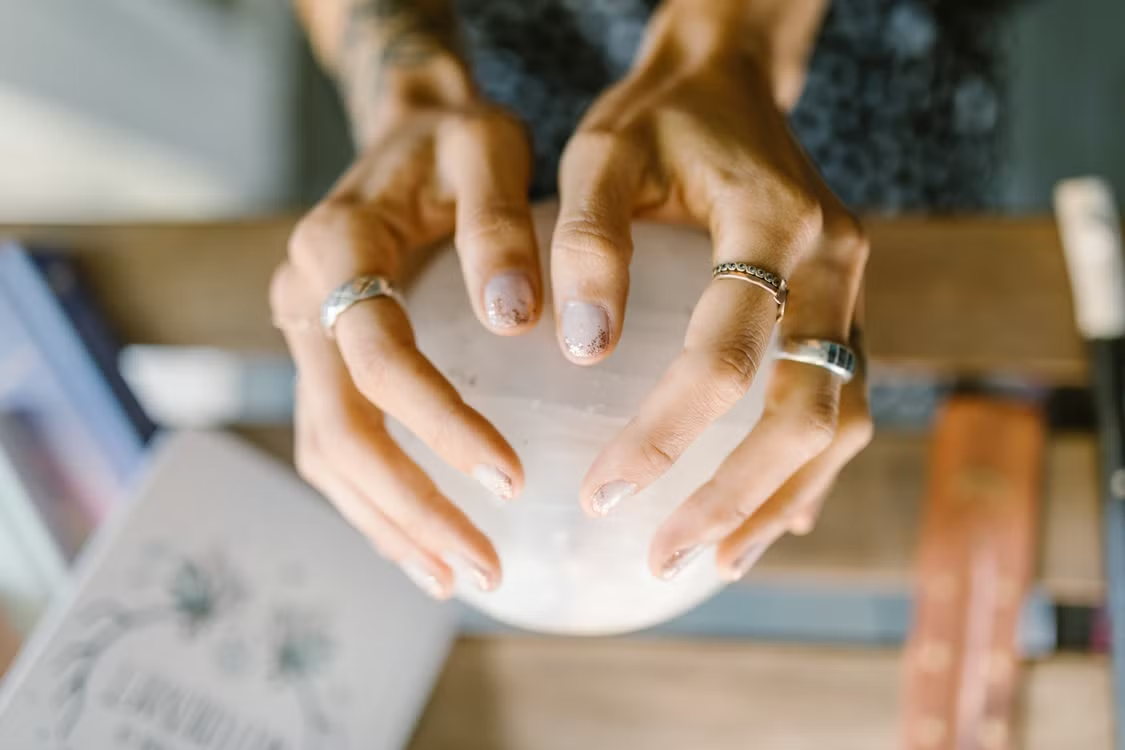 Ringed hands holding a clear crystal sphere symbolizing mediumship and spiritual healing practice.