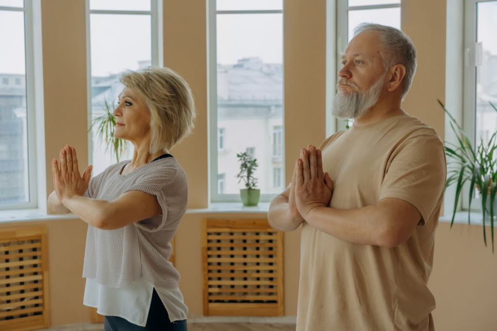 Middle-aged man and woman standing side by side in prayer pose during an indoor spiritual training session.