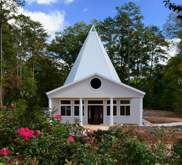White campus building with a peaked roof and columned porch surrounded by roses.