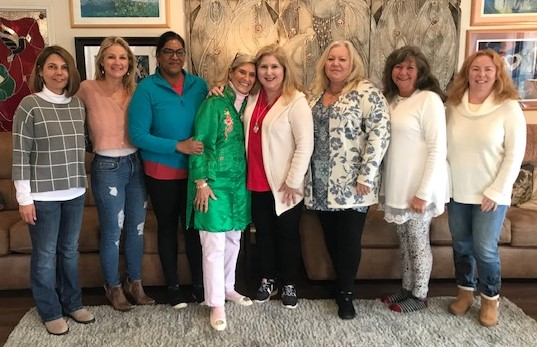 Eight women standing together in a common room for a group photo.