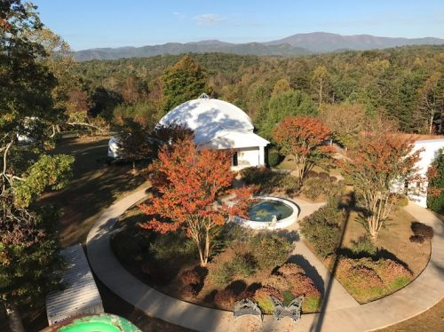 Aerial view of a white dome building with a fountain and mountain backdrop.